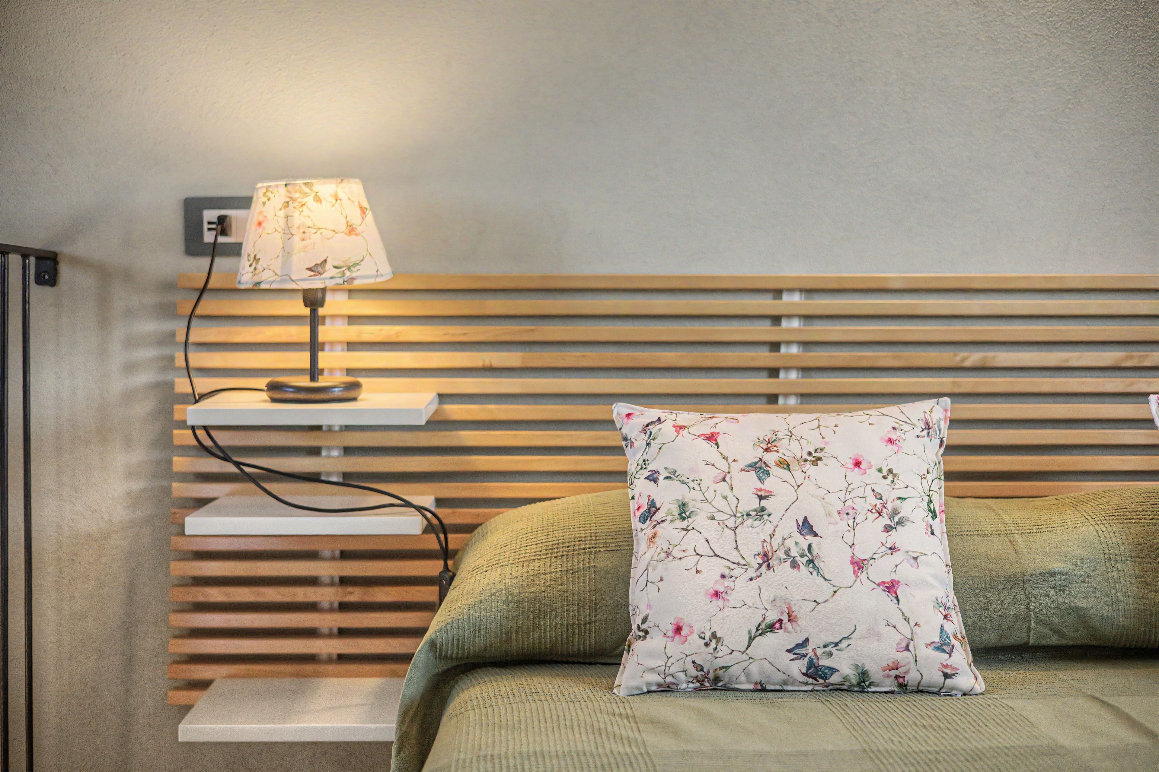 A bedroom with a bed, a nightstand, a lamp, and a wall-mounted shelf.