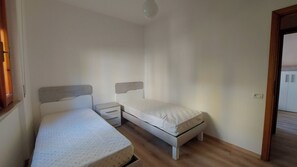 Quarto pequeno com uma cama de solteiro, piso de madeira, mesa de cabeceira e criado-mudo.