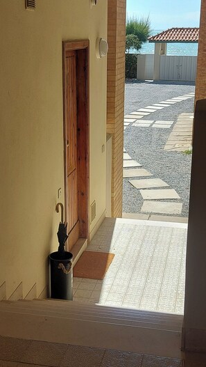 Blick aus einem Fenster auf einen gepflasterten Außenbereich mit einer Holztür und einer kleinen schwarzen Mülltonne.