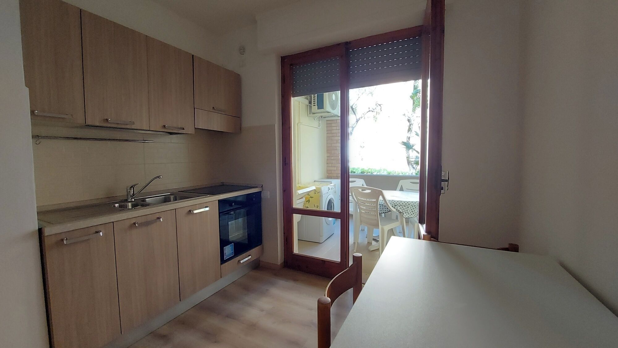 A compact kitchen with wooden cabinets, a built-in dishwasher, and a small dining area with a table and chairs.