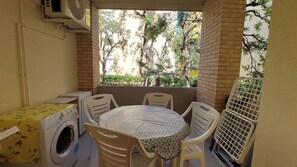Um pequeno pátio com uma mesa, cadeiras, máquina de lavar e ventilador.