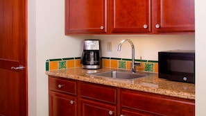 A kitchen with wooden cabinets, a stainless steel sink, a coffee maker, a microwave, and a tiled backsplash.