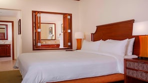 Una habitación de hotel con una cama grande, un cabecero de madera, una mesita de noche con lámpara y un espejo sobre la cama.