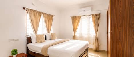 Un dormitorio con cama, ventilador de techo, aire acondicionado, armario de madera y una planta pequeña.