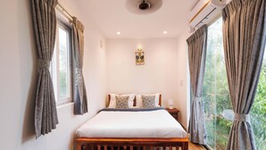 A bedroom with a bed, curtains, a bedside lamp, and a window with a view of greenery.