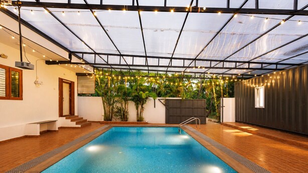 An indoor swimming pool with a glass ceiling, surrounded by wooden flooring and greenery.