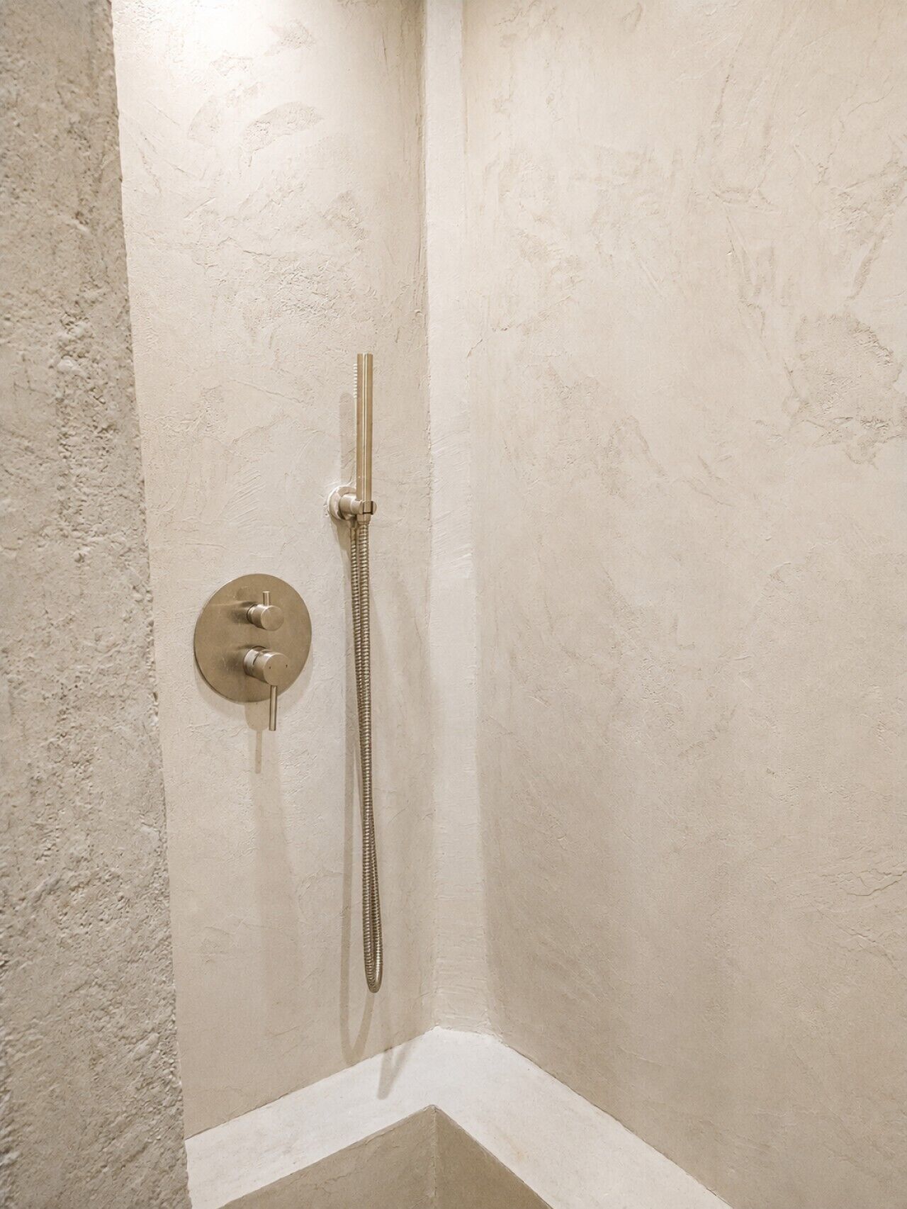 A corner shower with a handheld showerhead and a wall-mounted control panel.