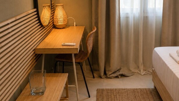 Een hotelkamer met een houten bureau, een stoel, een bed, een grote spiegel en een raam met gordijnen.