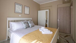 A bedroom with a bed, pillows, a bedside table, a wardrobe, and two framed pictures on the wall. - Blue Avra Suite by Rentals Pro - Nea Moudania Halkidiki (Nea Moudania)