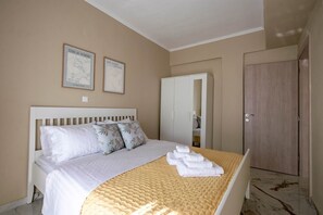 A bedroom with a bed, pillows, a bedside table, a wardrobe, and two framed pictures on the wall. - Blue Avra Suite by Rentals Pro - Nea Moudania Halkidiki (Nea Moudania)