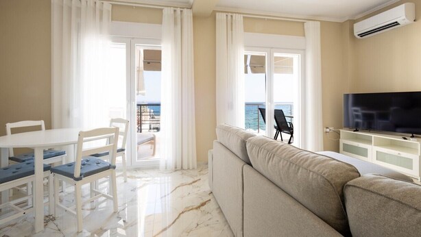 A hotel room with a balcony, a dining area, a sofa, and a television. - Blue Avra Suite by Rentals Pro - Nea Moudania Halkidiki (Nea Moudania)