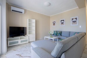 A modern living room with a flat-screen TV, a grey sofa, a white entertainment unit, and a small coffee table.