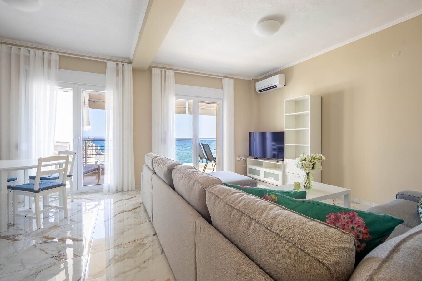 Uma sala de estar moderna com sofá, televisão de tela plana e varanda com vista para o mar.