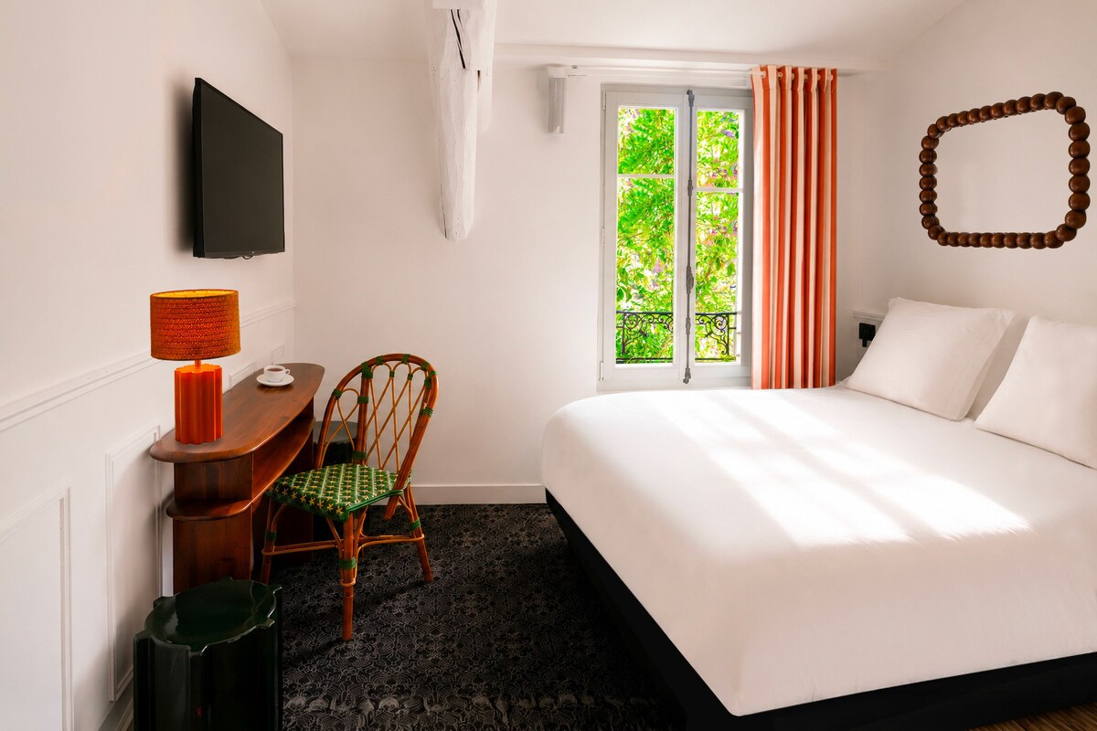 Ein Hotelzimmer mit einem Bett, einem Schreibtisch mit Stuhl, einem Fernseher und einem Fenster mit Vorhängen.