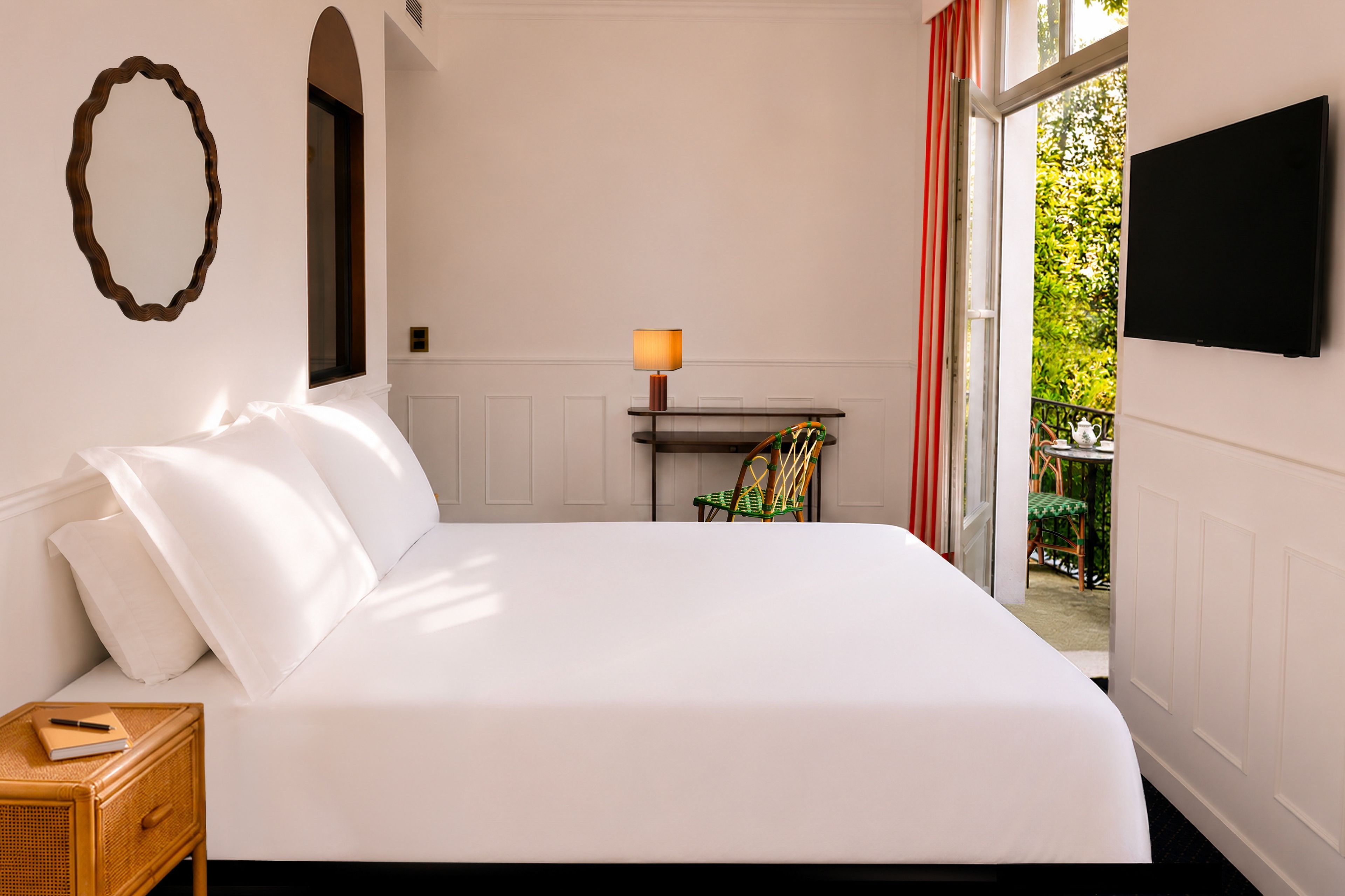 A hotel room with a large bed, a bedside table with a lamp, a chair, and a TV mounted on the wall.