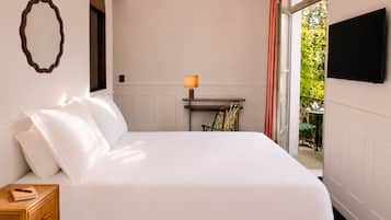 A hotel room with a large bed, a bedside table with a lamp, a chair, and a TV mounted on the wall.