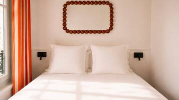 A hotel room with a bed, two bedside tables, a wall-mounted decorative object, and a window with curtains.