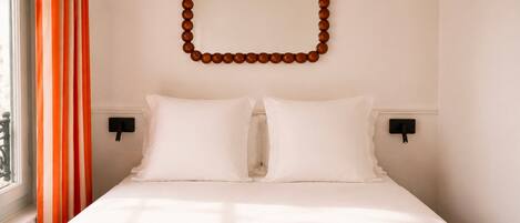A hotel room with a bed, two bedside tables, a wall-mounted decorative object, and a window with curtains.