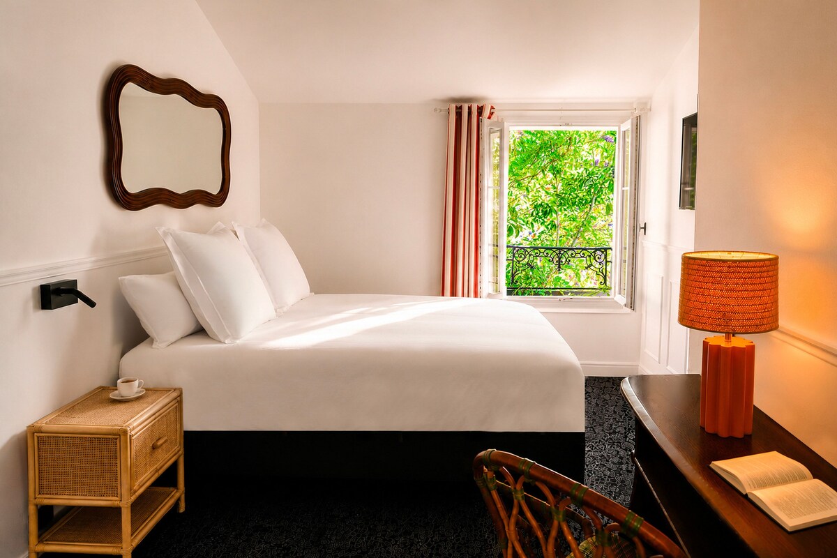 Ein Hotelzimmer mit einem Bett, einem Nachttisch mit Lampe, einem Sessel, einem Fenster mit Vorhängen und einem Spiegel an der Wand.