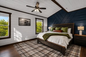 A bedroom with a bed, a ceiling fan, a nightstand, a lamp, and a window with a view of greenery. - Indoor Pool! Luxury Design, Game Room, Hot Tub! (Sevierville)