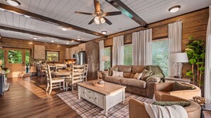 A spacious living area with a wooden ceiling, a ceiling fan, a sofa, a coffee table, and a dining area with a wooden table and chairs. - Indoor Pool! Luxury Design, Game Room, Hot Tub! (Sevierville)