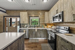 A modern kitchen with wooden cabinetry, a stainless steel stove, and a microwave. - Indoor Pool! Luxury Design, Game Room, Hot Tub! (Sevierville)