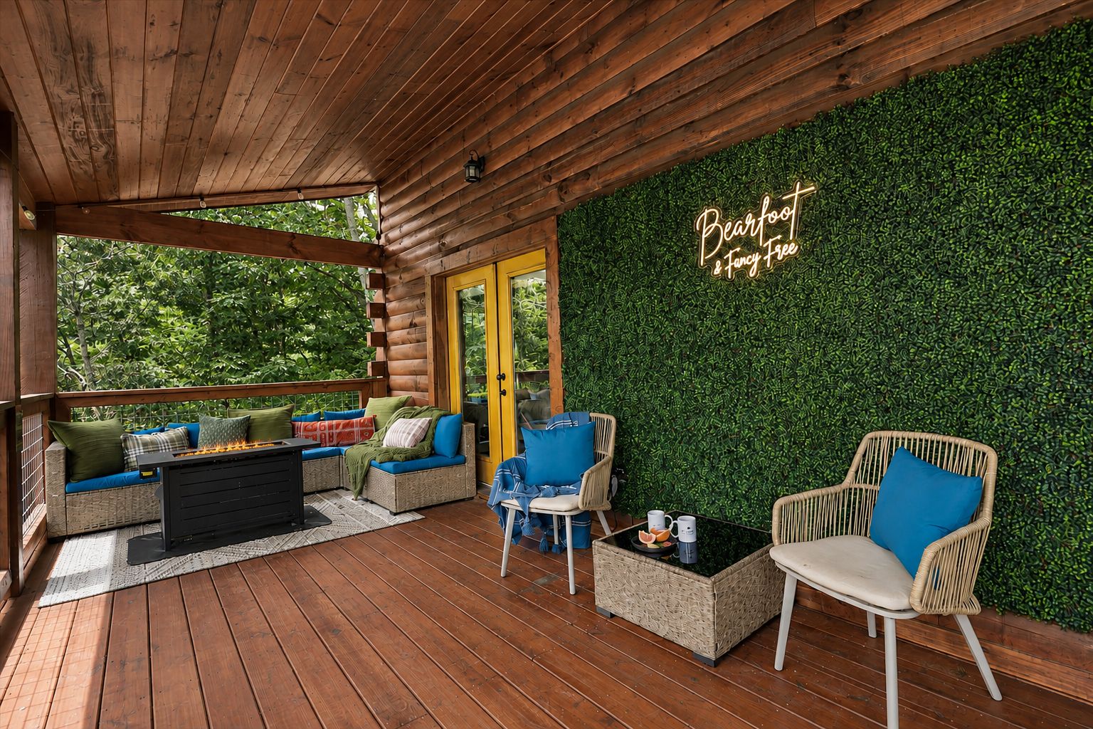 A wooden deck with outdoor seating, a fire feature, and a wall with a green hedge and a neon sign.