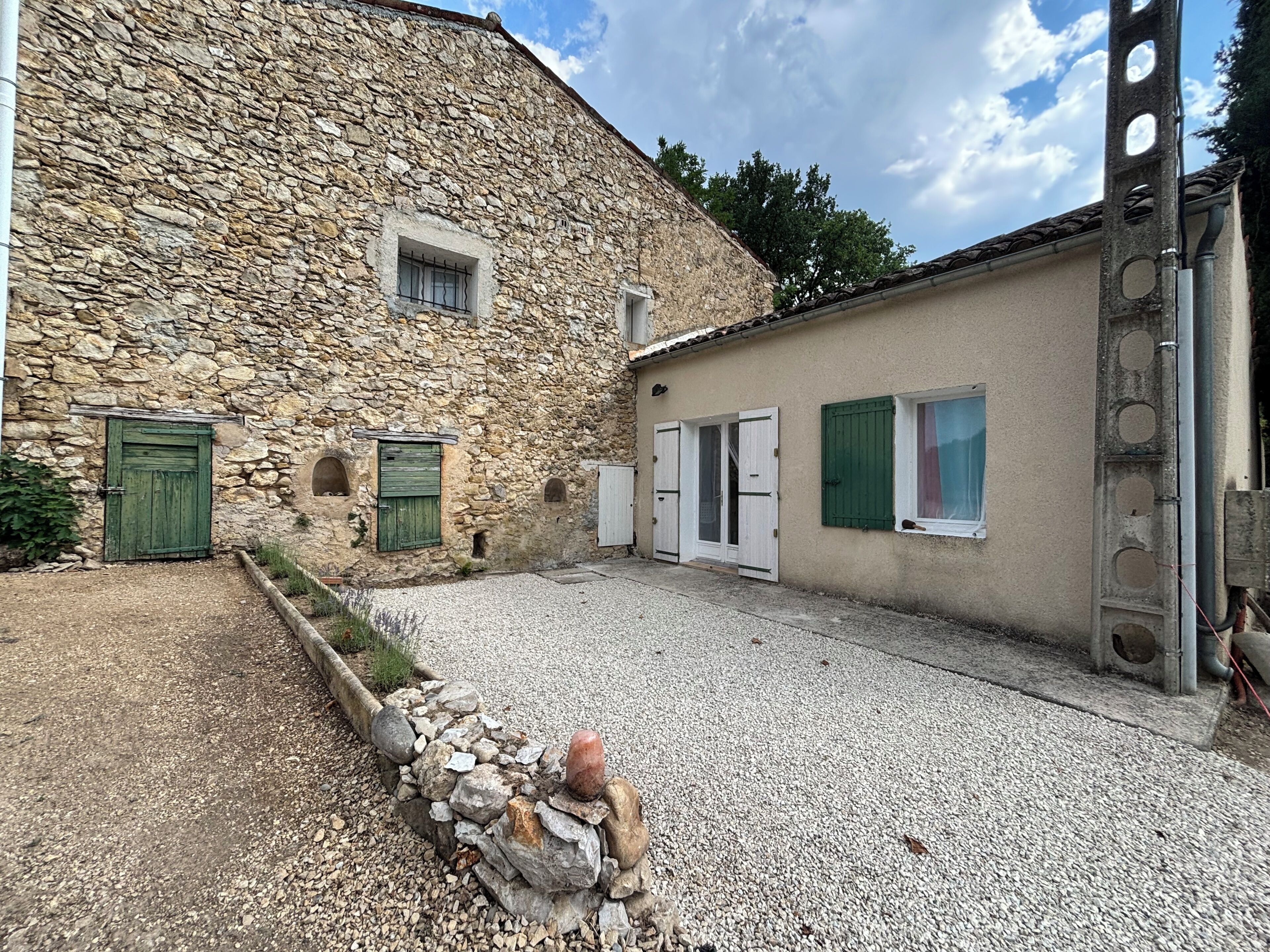 A stone building with a gravel courtyard, a green door, and a window with shutters.