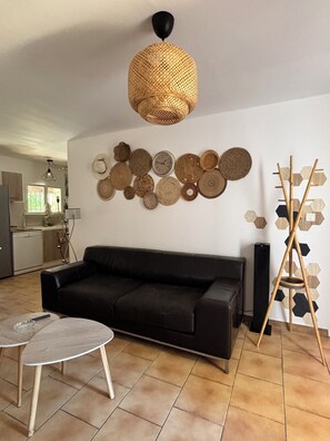 A living room with a black sofa, a round coffee table, a woven pendant light, and a wall decorated with woven baskets and a wooden hexagon pattern.