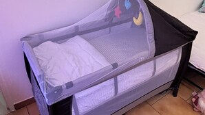En spjälsäng med ett myggnät och en madrass, placerad intill en vägg med ett kaklat golv.