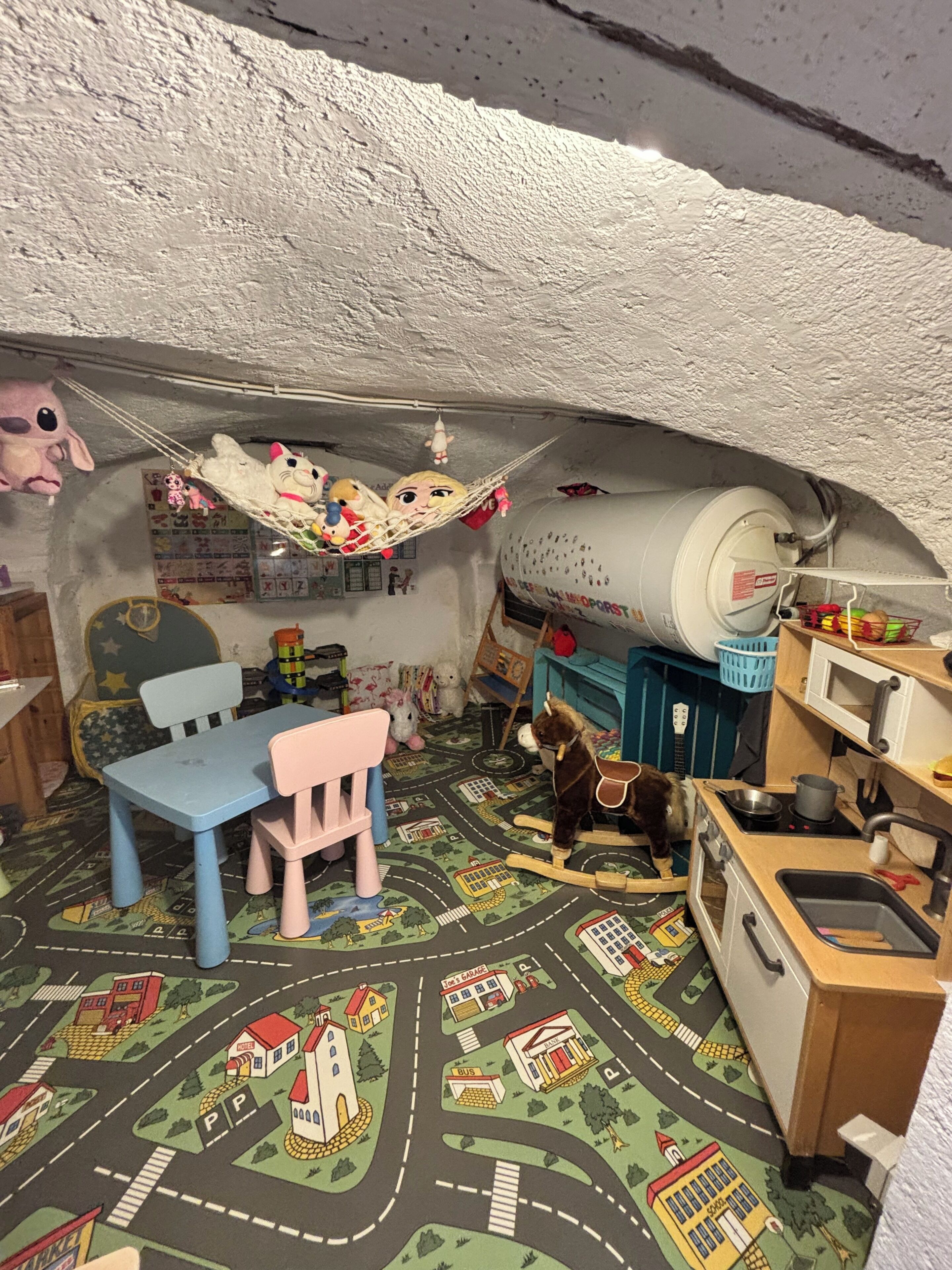 A play kitchen with a toy stove, sink, and a mat with a town layout.