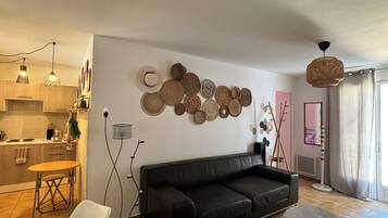 A modern living room with a black leather sofa, a dining area with a round table, and a kitchen in the background.