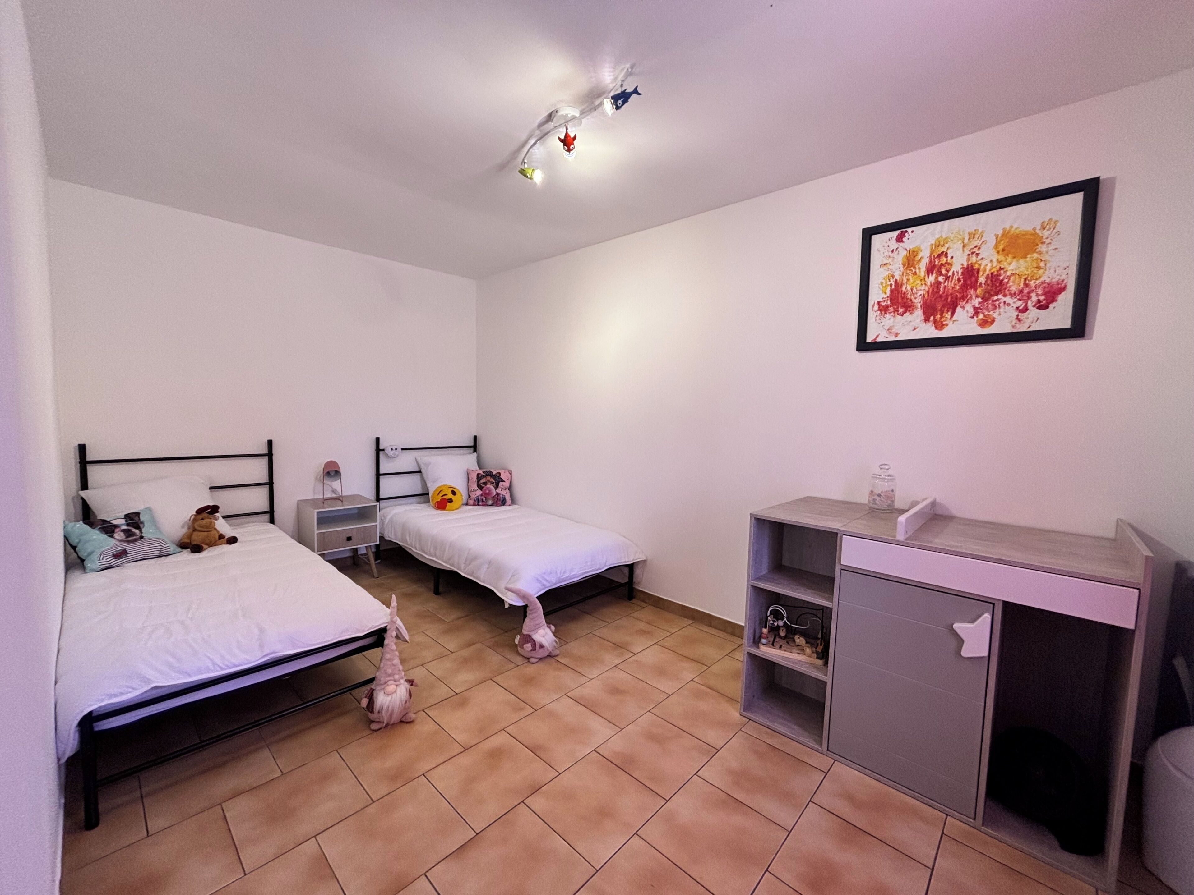 A bedroom with two beds, a desk, and a shelf unit.