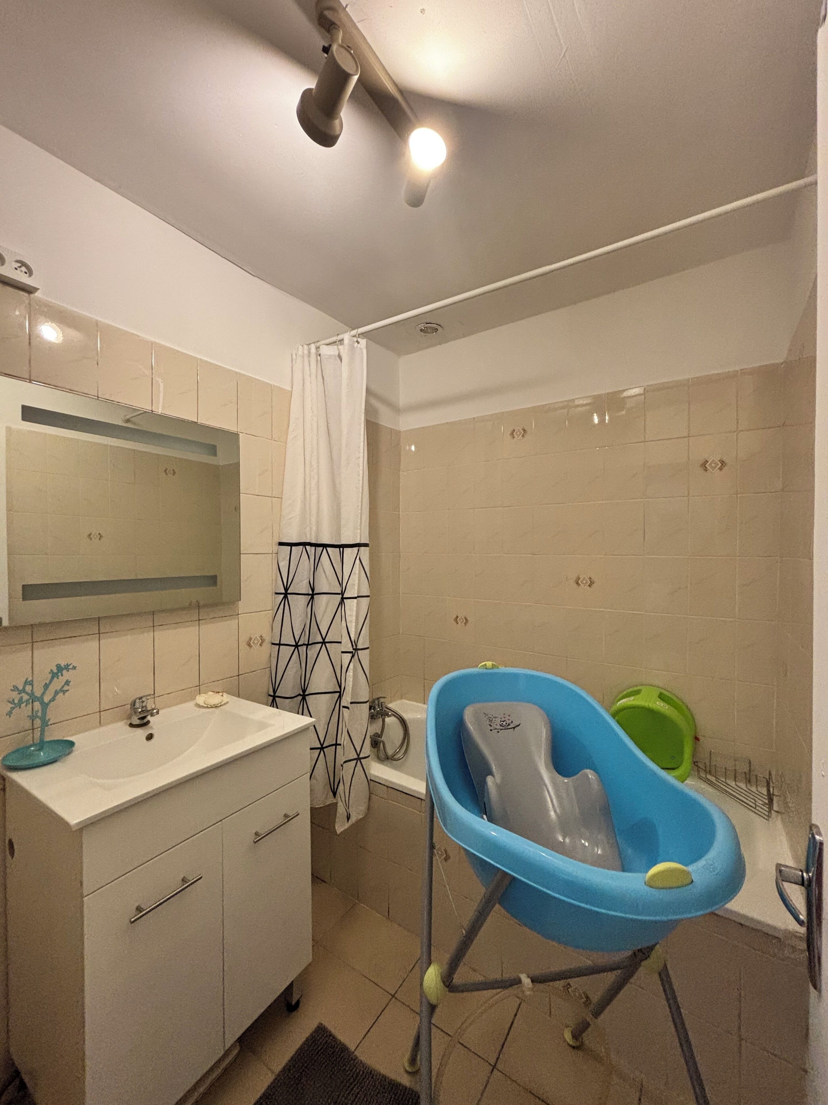 Une salle de bain avec un lavabo blanc, un miroir et une petite baignoire bleue pour bébé.