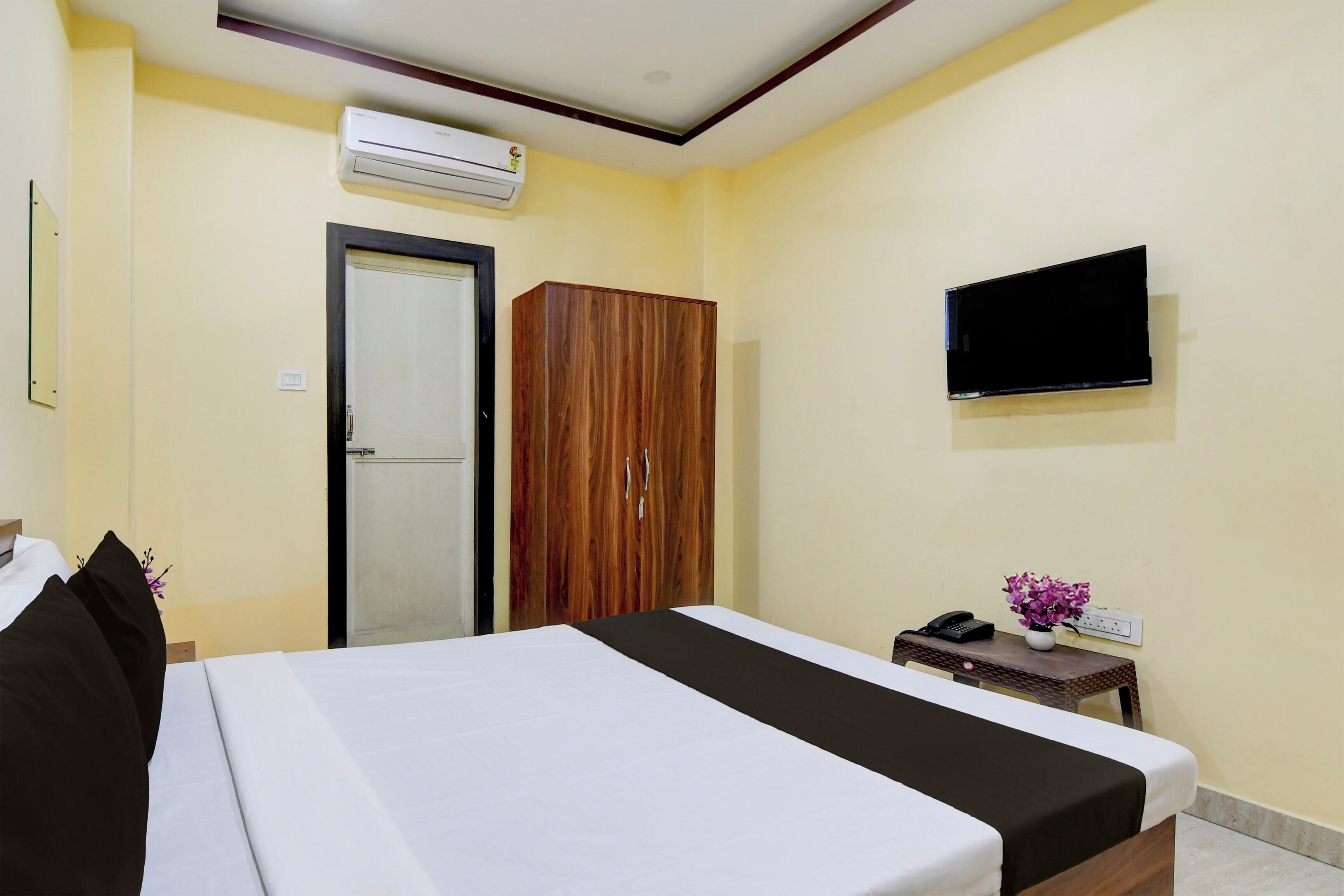 Habitación de hotel con cama, armario, televisor y una mesita con teléfono y un florero.