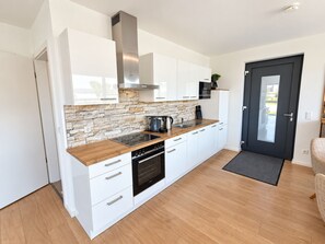 A modern kitchen with white cabinets, a stone backsplash, and a black stove. - Holiday apartment with infrared sauna, fireplace & terrace in Winterberg (Winterberg)