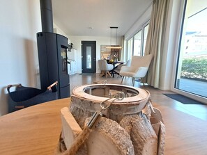 A modern living room with a large wooden table, a black cylindrical object, and a view of the kitchen and dining area through an open door. - Holiday apartment with infrared sauna, fireplace & terrace in Winterberg (Winterberg)