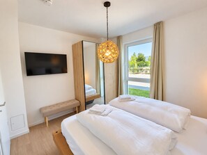 A modern hotel room with a large bed, a bench, a television, and a view of the outdoors. - Holiday apartment with infrared sauna, fireplace & terrace in Winterberg (Winterberg)