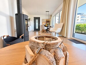 A modern living room with a large wooden table, a black wood-burning stove, and a view of the city through large windows. - Holiday apartment with infrared sauna, fireplace & terrace in Winterberg (Winterberg)