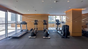 A modern gym with treadmills, elliptical machines, and stationary bikes. Large windows provide views of the cityscape. - Maison Privee - Elegant Studio Retreat in Damac Hills (Dubai)