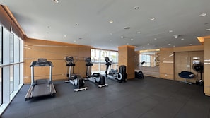 A modern gym with various cardio machines, a bench, and a fan. - Maison Privee - Elegant Studio Retreat in Damac Hills (Dubai)