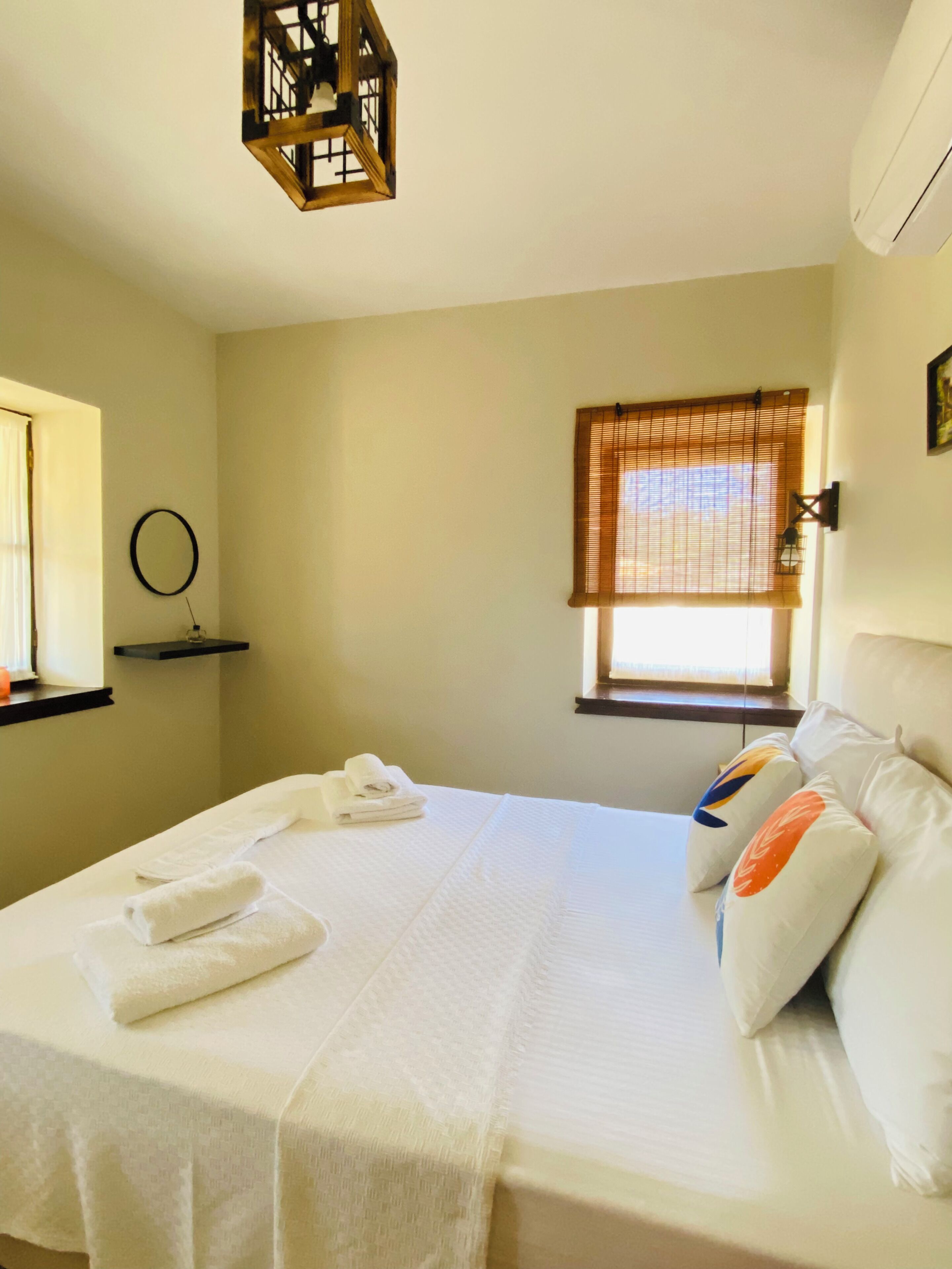 A hotel room with a bed, towels, a window with blinds, a wall-mounted light fixture, and a ceiling light.