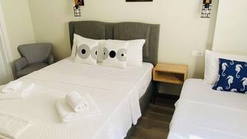 Habitación de hotel con dos camas, cabecero gris, aire acondicionado de pared, mesita de noche pequeña y una silla.