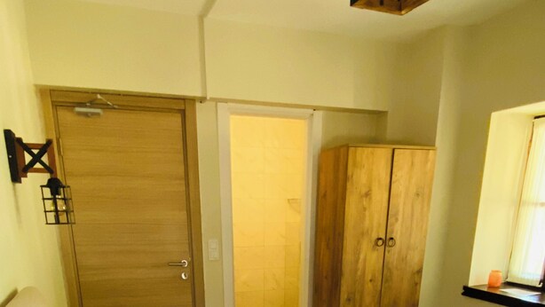 A hotel room with a bed, a red chair, a wardrobe, and a bathroom visible through an open door. - Baraka Bozcaada (Bozcaada)