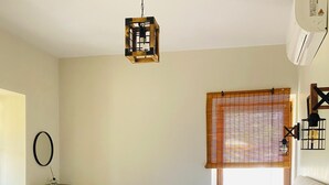 A bedroom with a bed, a red chair, a hanging light fixture, a window with blinds, and a wall-mounted air conditioner. - Baraka Bozcaada (Bozcaada)