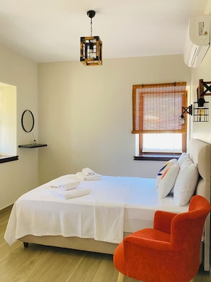 A bedroom with a bed, a red chair, a hanging light fixture, a window with blinds, and a wall-mounted air conditioner.