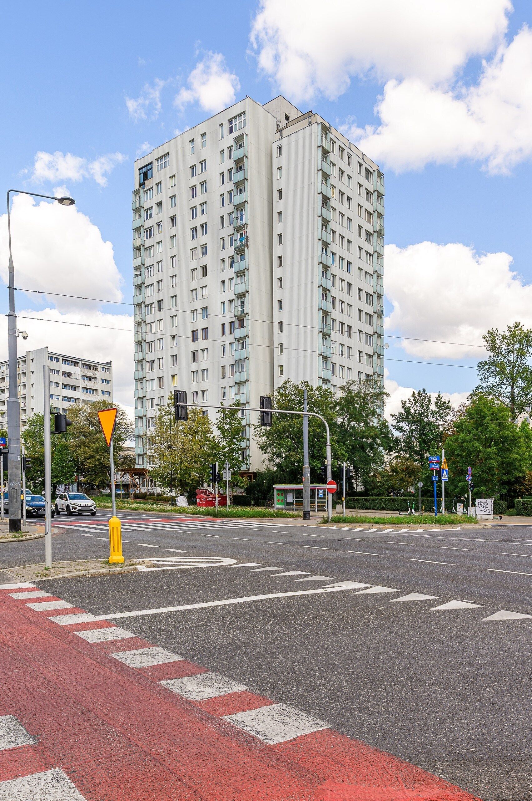 Un immeuble à étages doté d’une architecture moderne, situé à un carrefour où se trouvent des feux de signalisation et des marquages au sol.