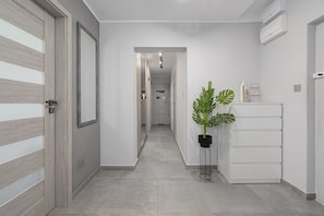 Een hal met een houten deur, een potplant en een witte kast.