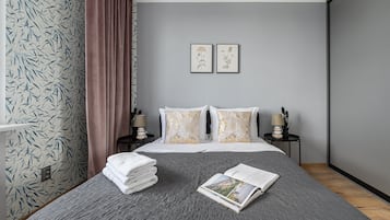 A hotel room with a bed, two bedside tables with lamps, a window with curtains, and a wall with framed botanical prints.