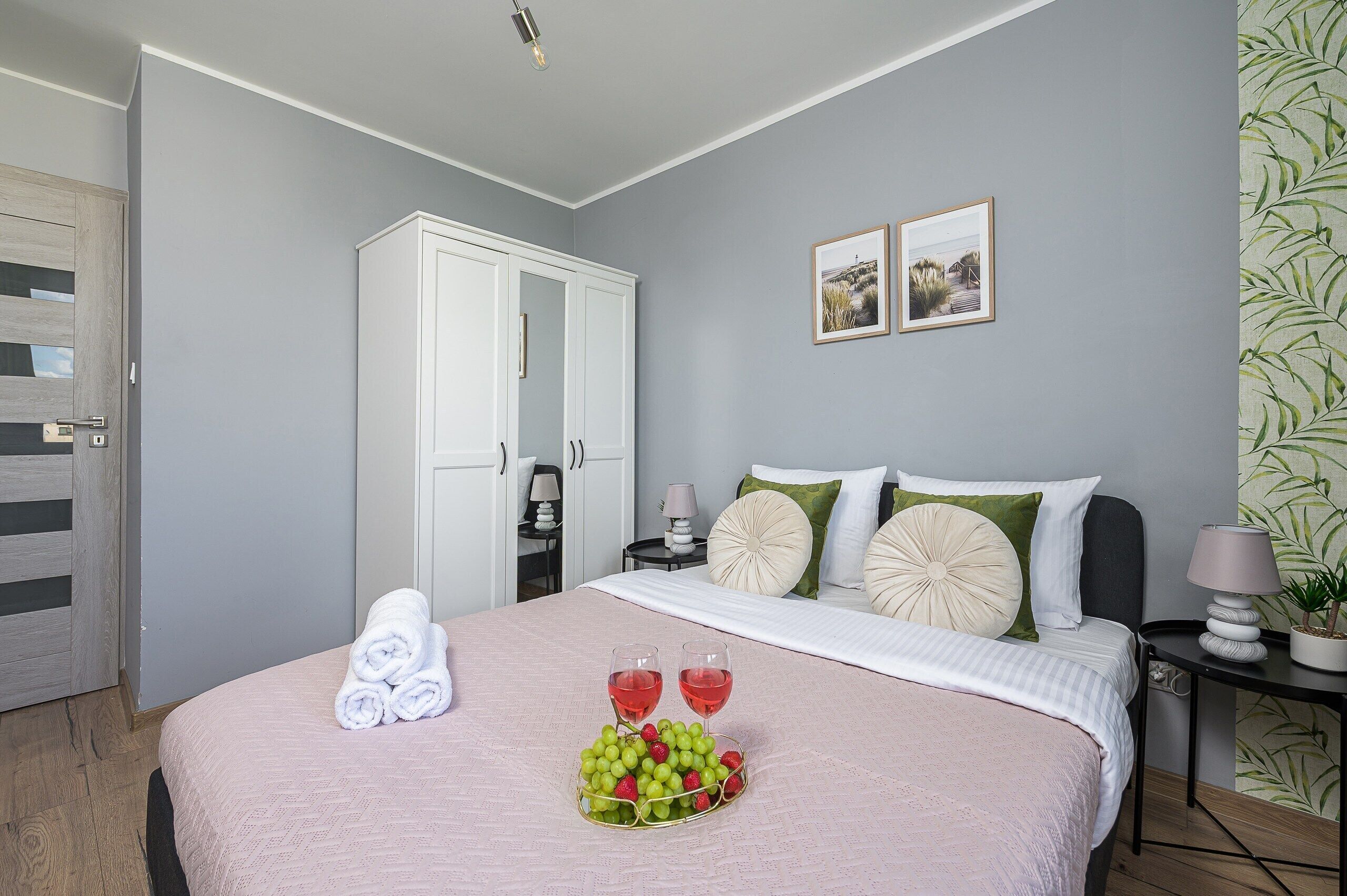 A hotel room with a bed, a wardrobe, a bedside table, a lamp, and a wall with two framed pictures.
